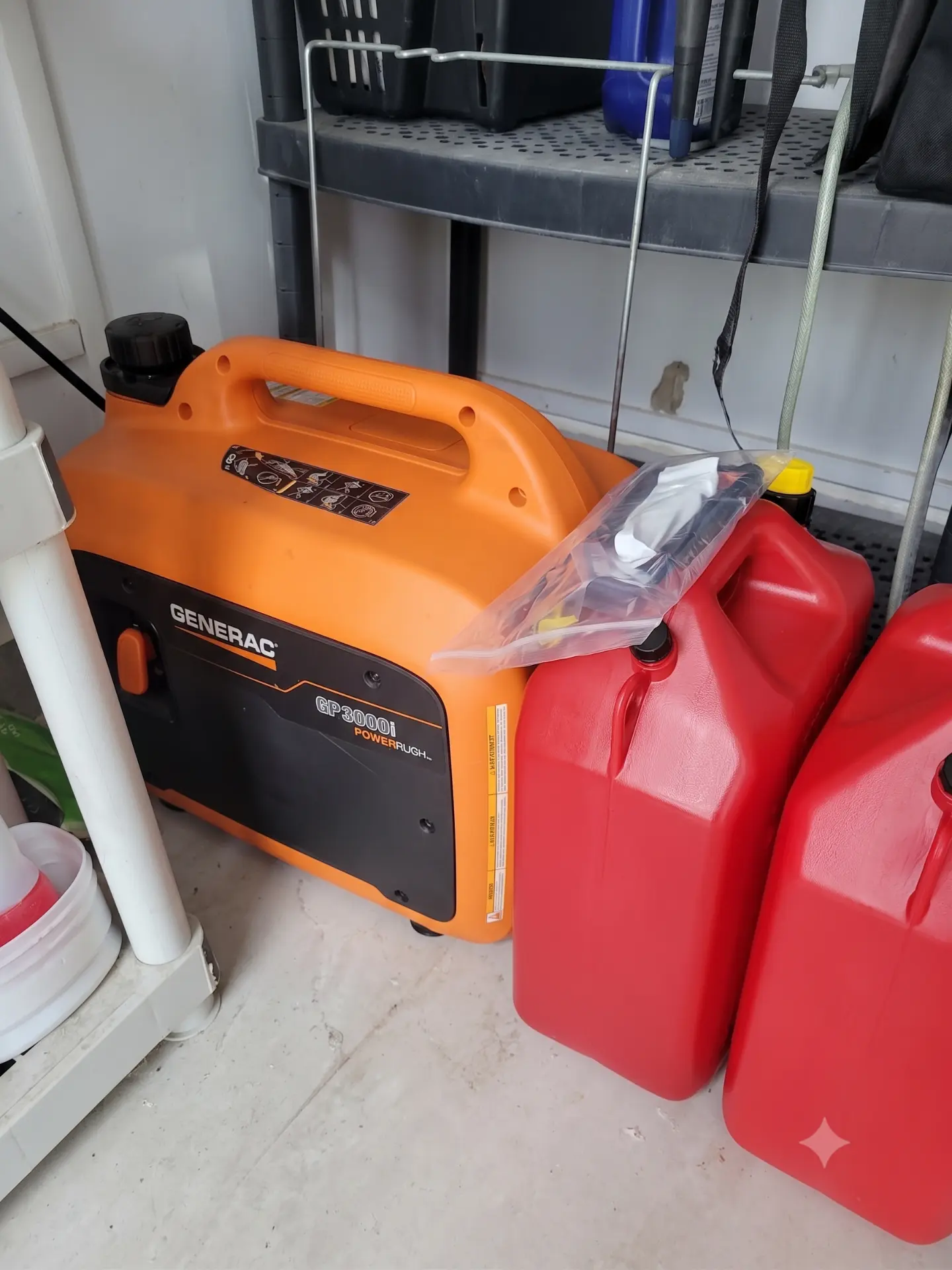 A Generac GP3000i portable inverter generator stored beside two red fuel containers
